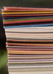 A side view of a tall stack of magazines, revealing the spines and covers with vibrant colors and diverse titles.